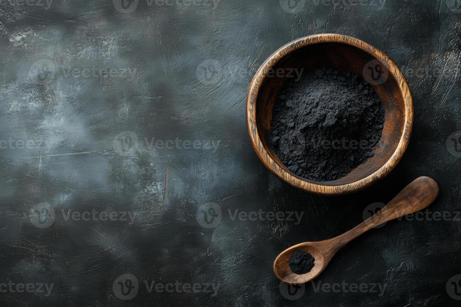 Activated charcoal powder in a wooden bowl with a spoon against a black background for natural wellness and beauty applications photo