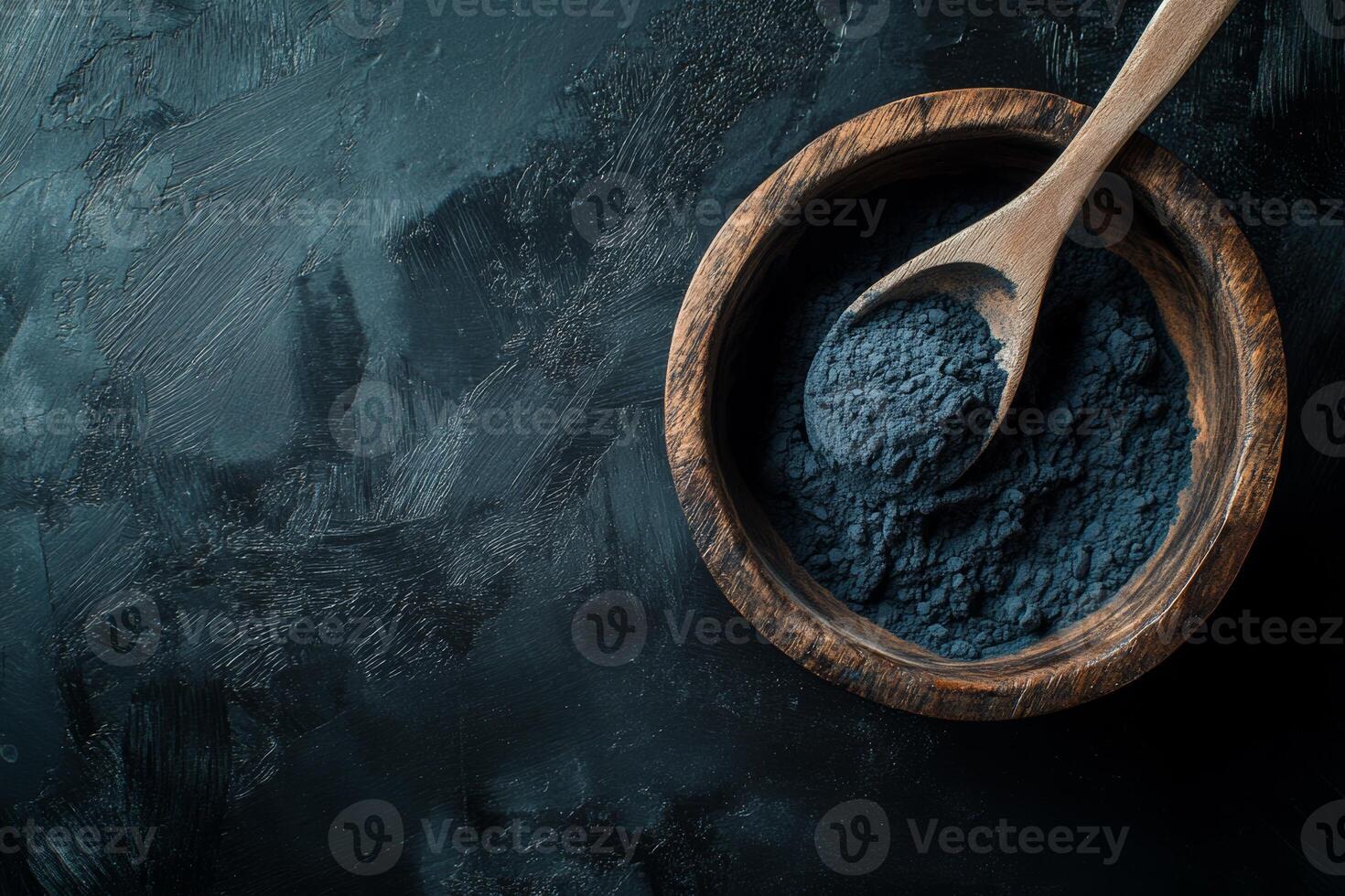 Activated charcoal powder displayed in a wooden bowl with a spoon against a black textured background photo
