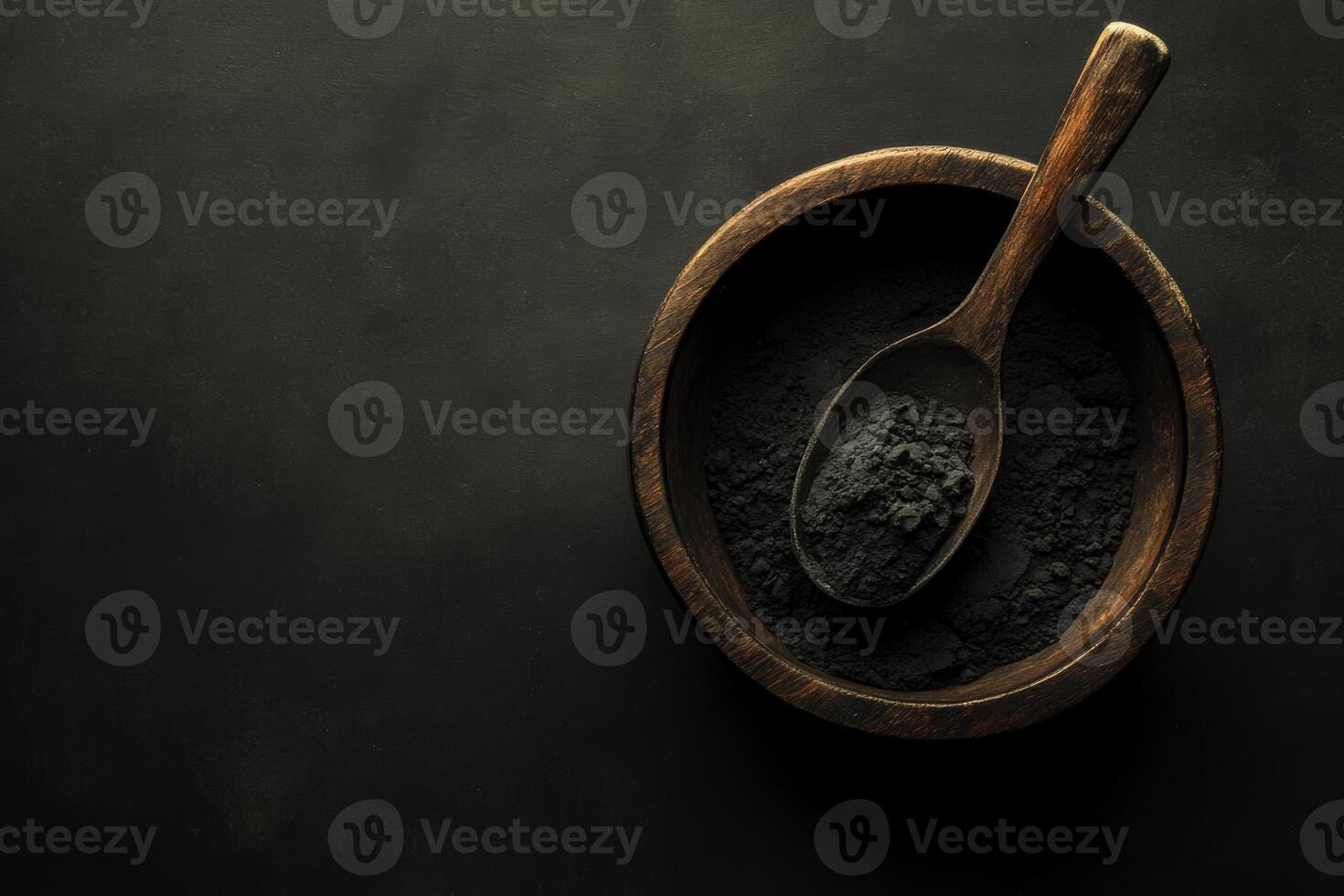 Activated charcoal powder in a wooden bowl with a spoon on a black background showcasing natural ingredients for wellness photo