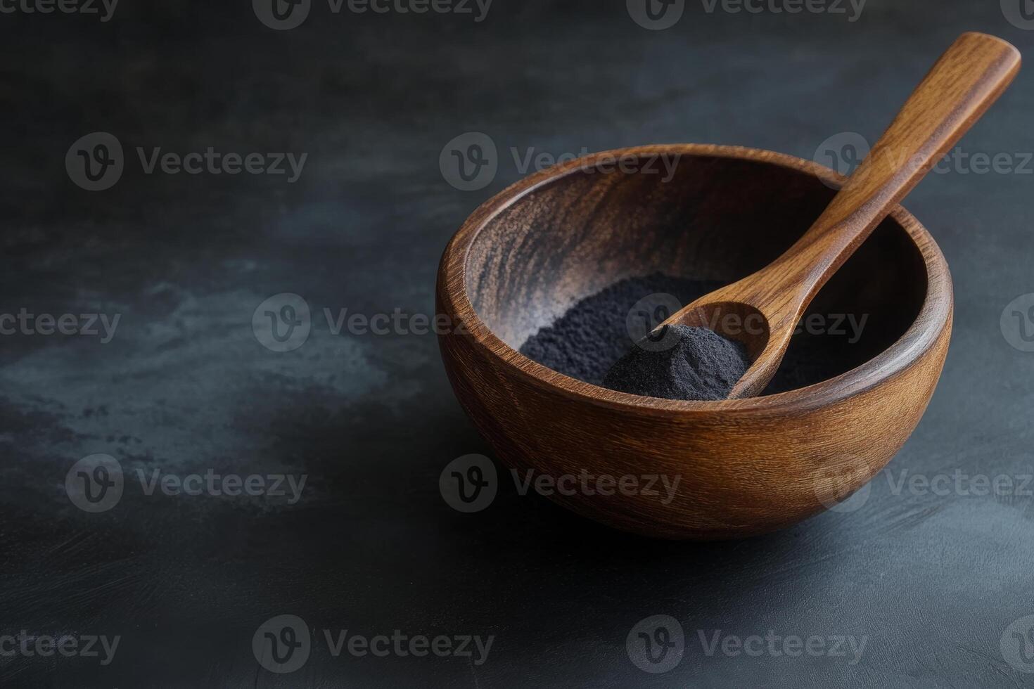 Activated charcoal powder displayed in a wooden bowl with a spoon on a textured black background, emphasizing its natural appeal photo