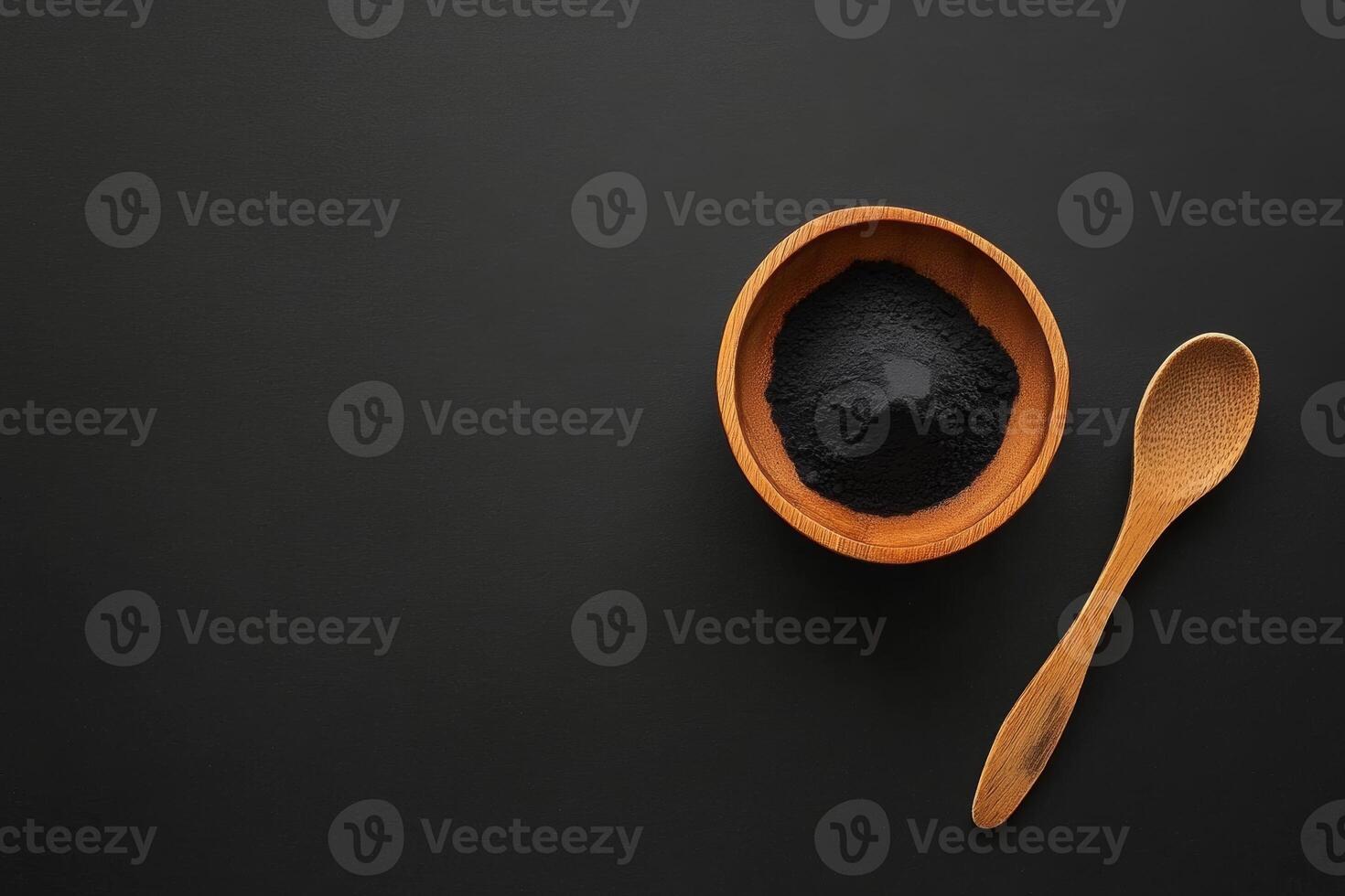 Activated charcoal powder in a wooden bowl with a spoon on a black background for natural health and beauty applications photo