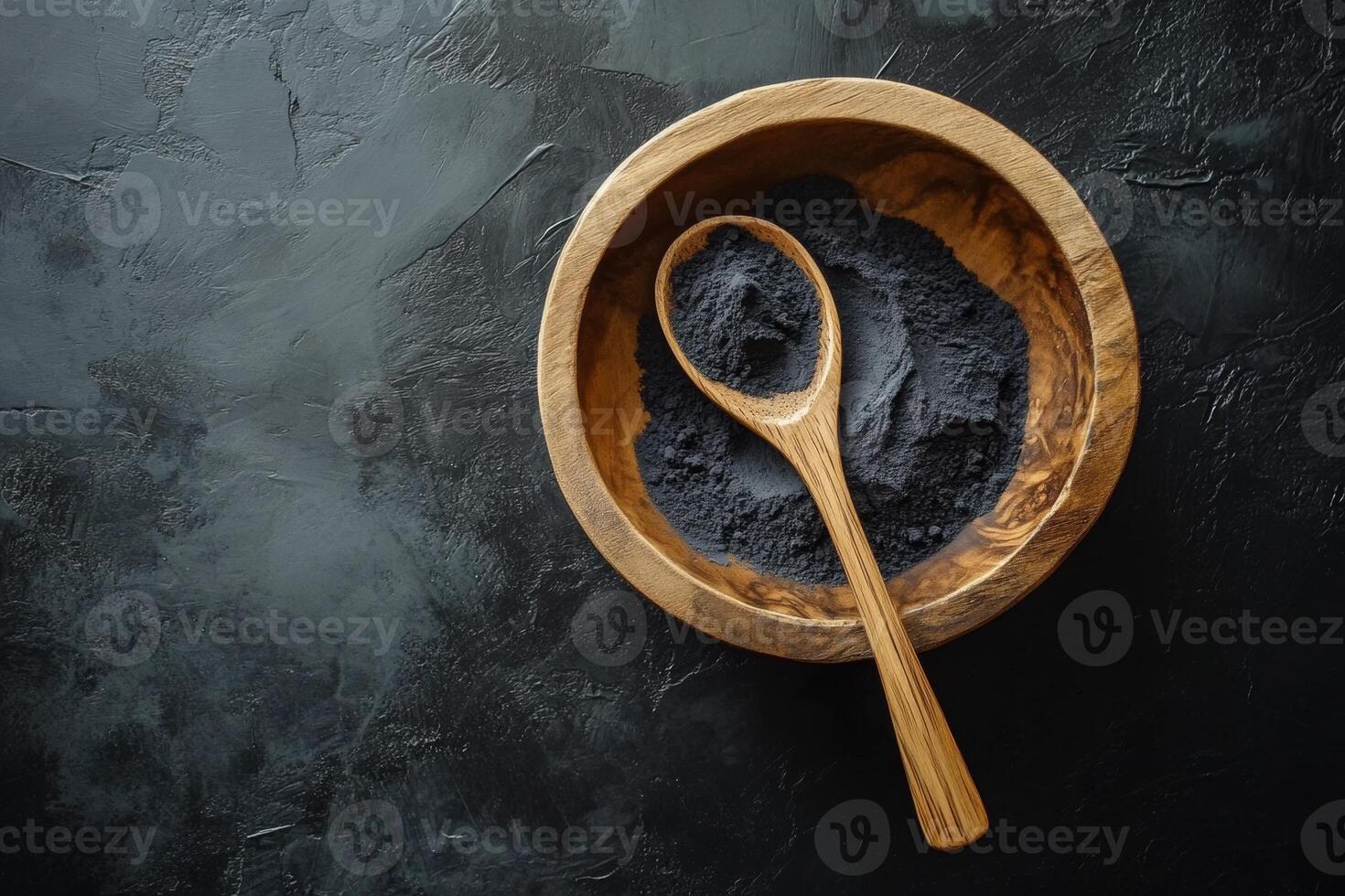 Activated charcoal powder in a wooden bowl with a spoon set against a sleek black background for natural health and beauty remedies photo