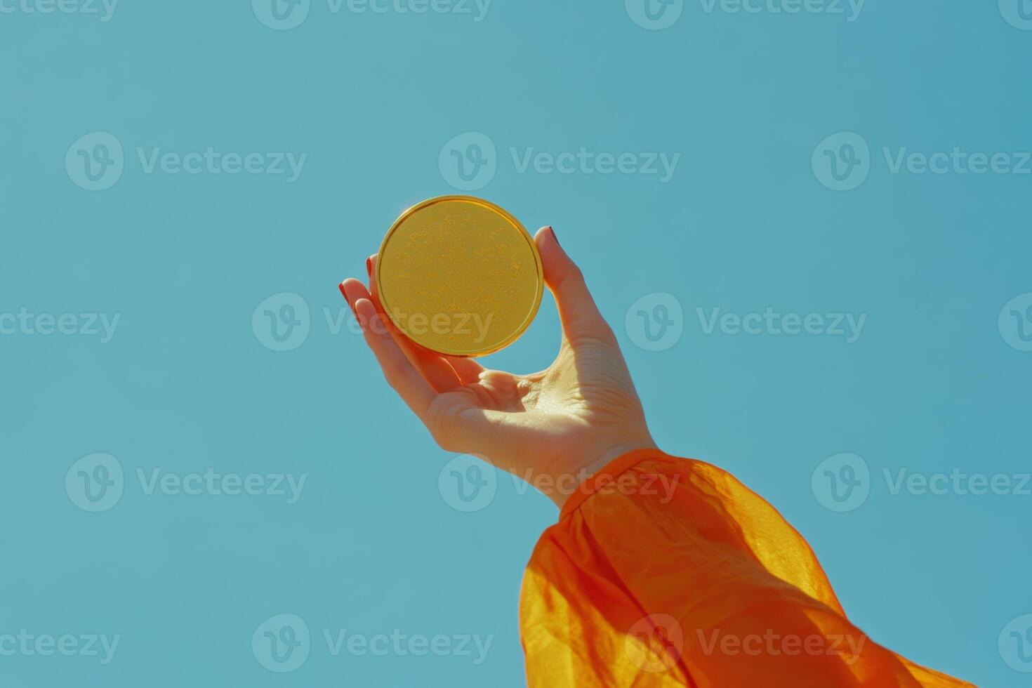 A hand proudly displays a gold medal against a bright blue sky, celebrating achievement and triumph in a moment of victory photo
