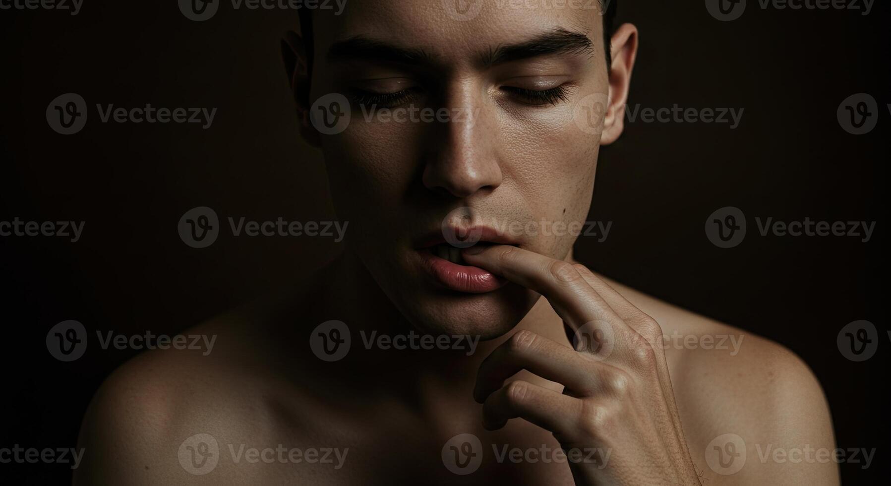 Introspective young man with finger on lips in moody, dark studio shot photo