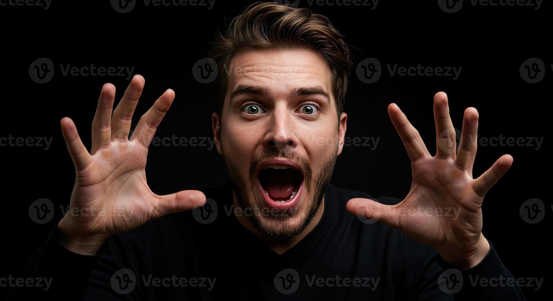 Man reacting in shock with open mouth and hands up against dark background photo