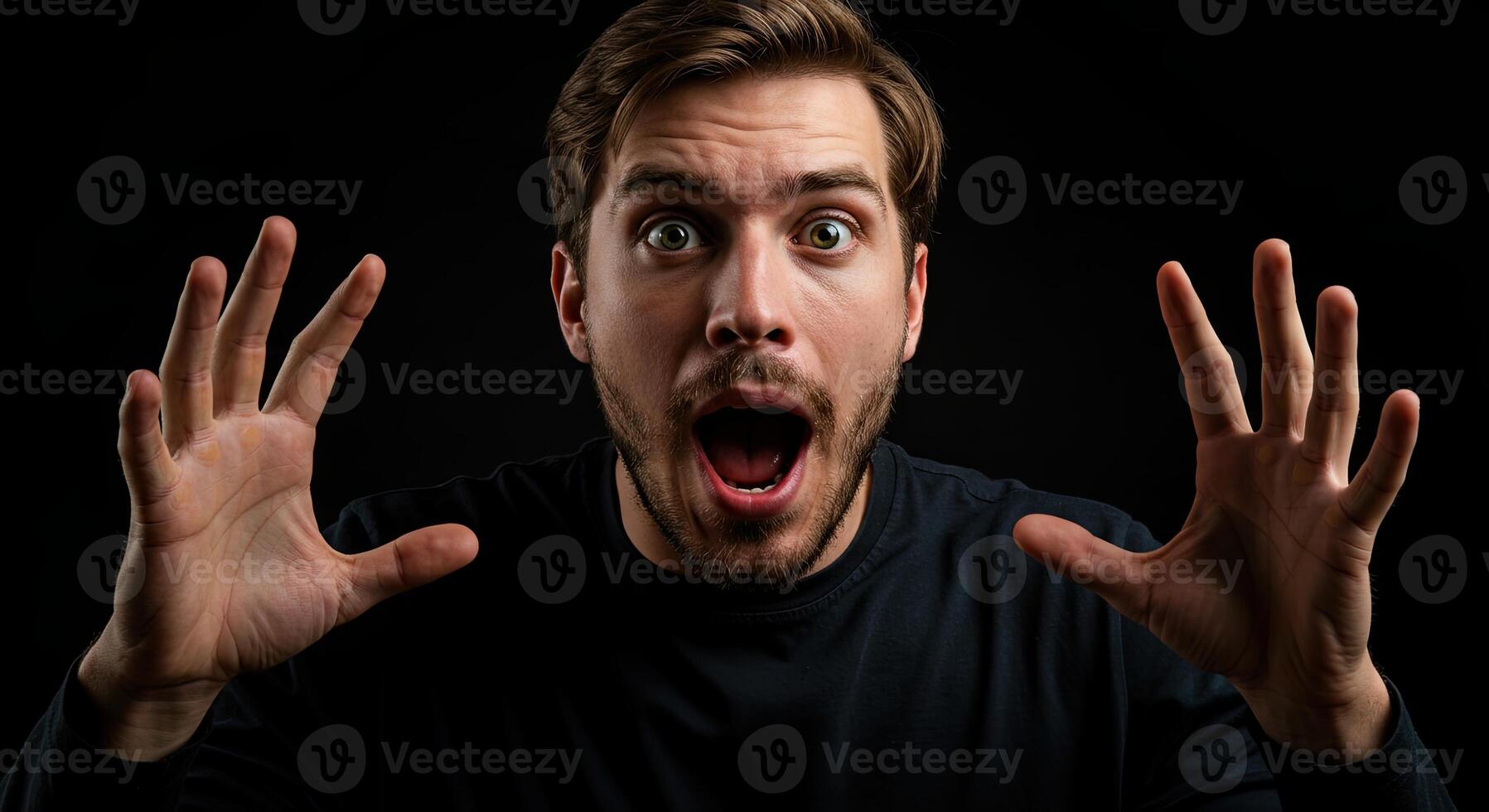 Man with surprised expression raises hands in disbelief against black background photo