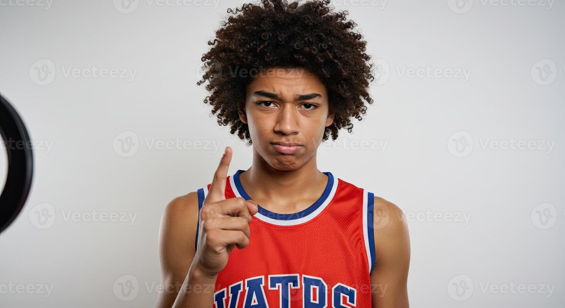 Serious teenager with afro wearing basketball jersey raising finger up photo