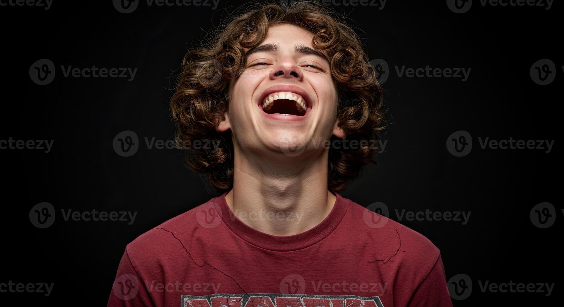 Young man with curly hair laughing heartily against a black background photo