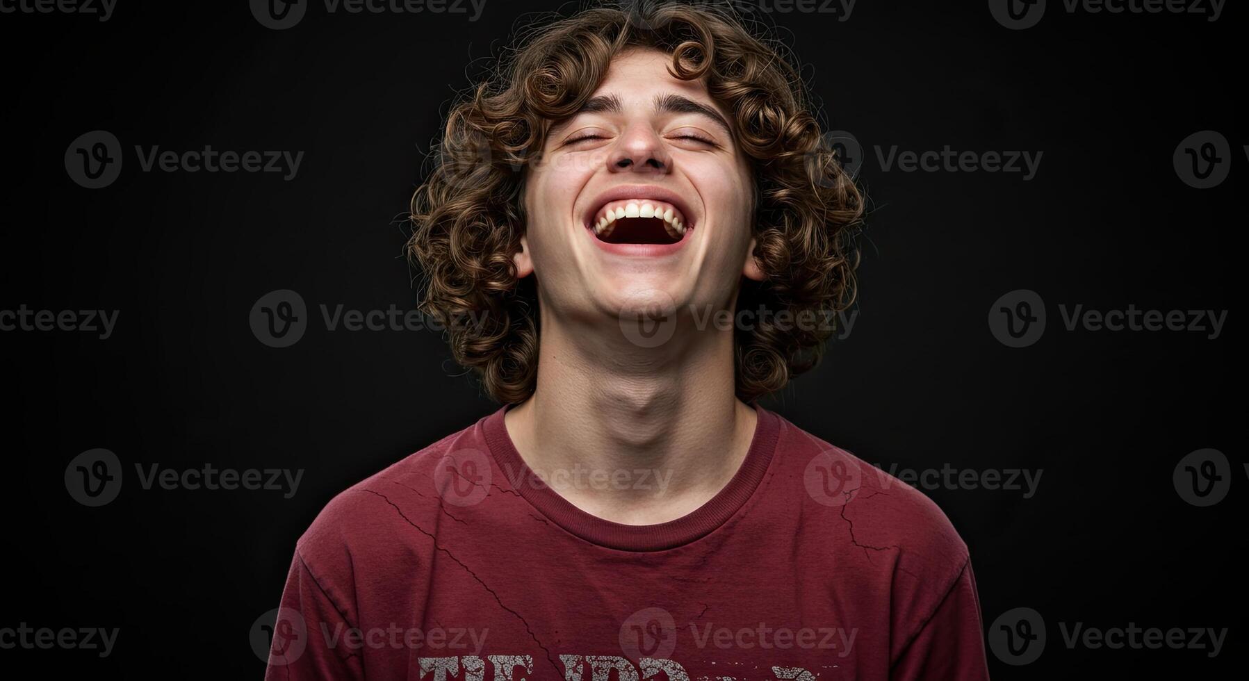 Young man with curly hair laughing joyfully against a dark background photo