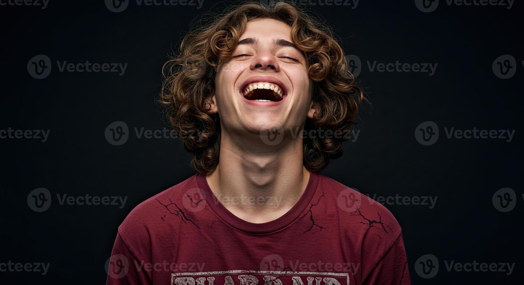 Young man with curly hair laughing joyfully eyes closed studio shot photo