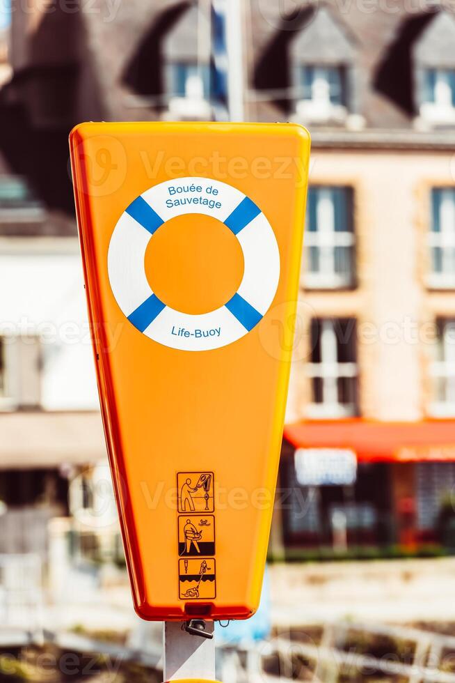 Life buoy in bright orange container by quaint buildings, safety concept photo