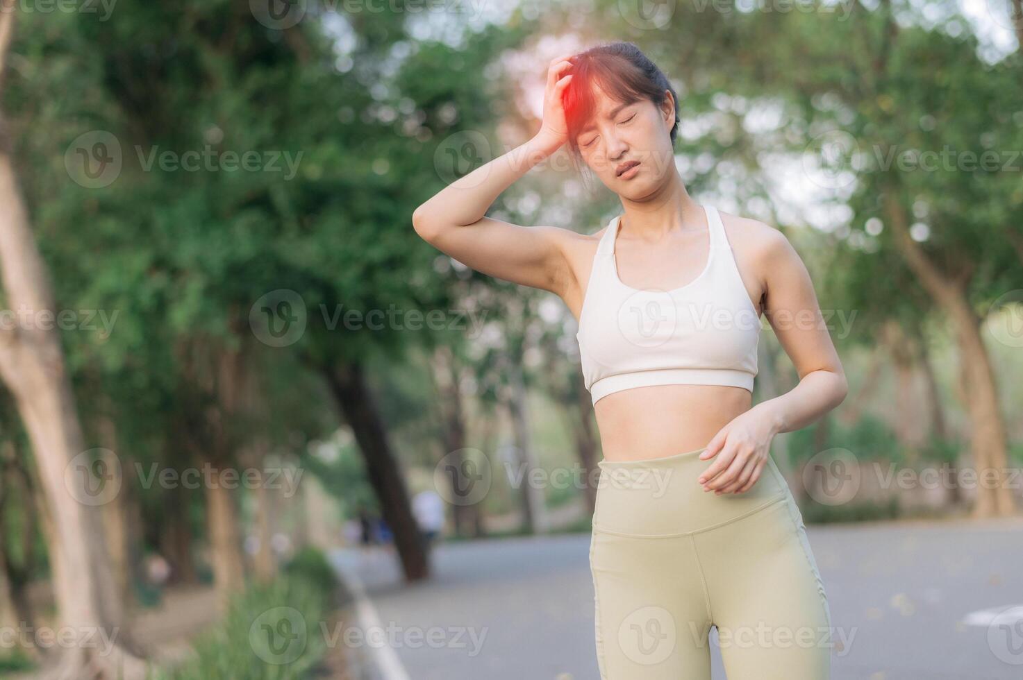 Sport southeast asian female teen jogging running health public park pain during exercise as she stops and touches her head with pained expression in green outdoor setting photo