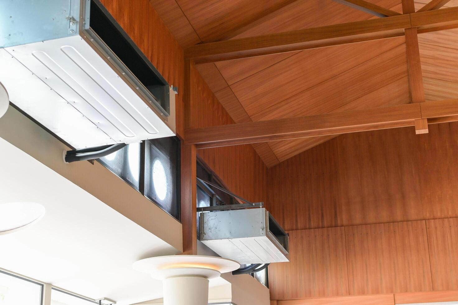 Close up view of modern HVAC duct system installed against wooden vaulted ceiling with exposed beams in bright interior space showing architectural details and ventilation components photo