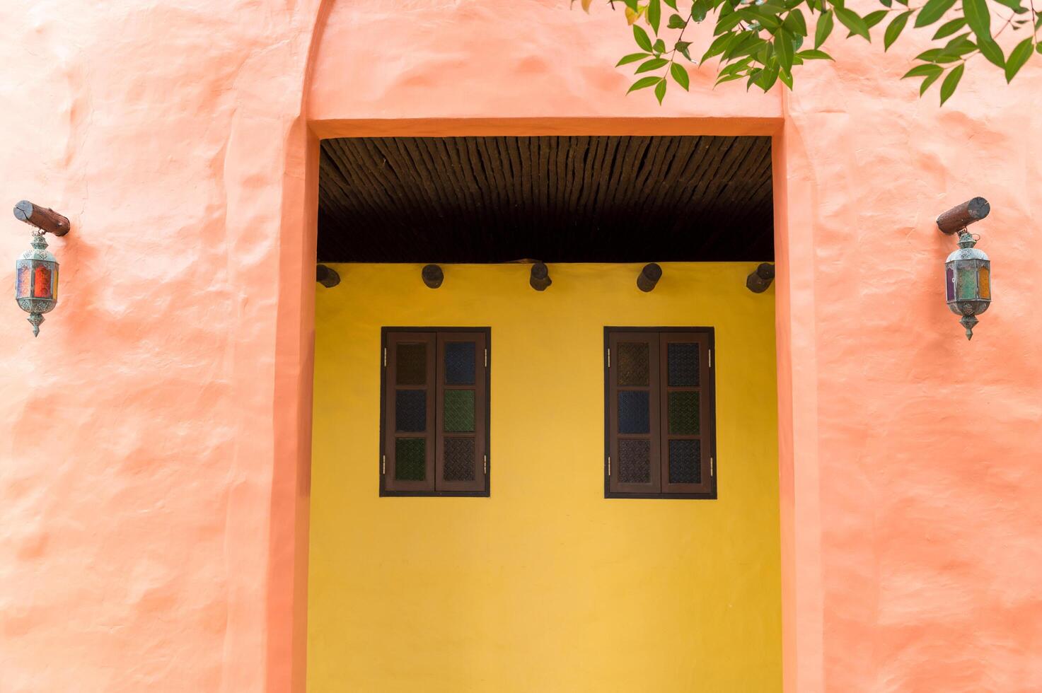 Moroccan inspired doorway featuring stained glass panes and vibrant yellow walls creating colorful and inviting entrance with rustic lanterns and natural wooden ceiling beams photo