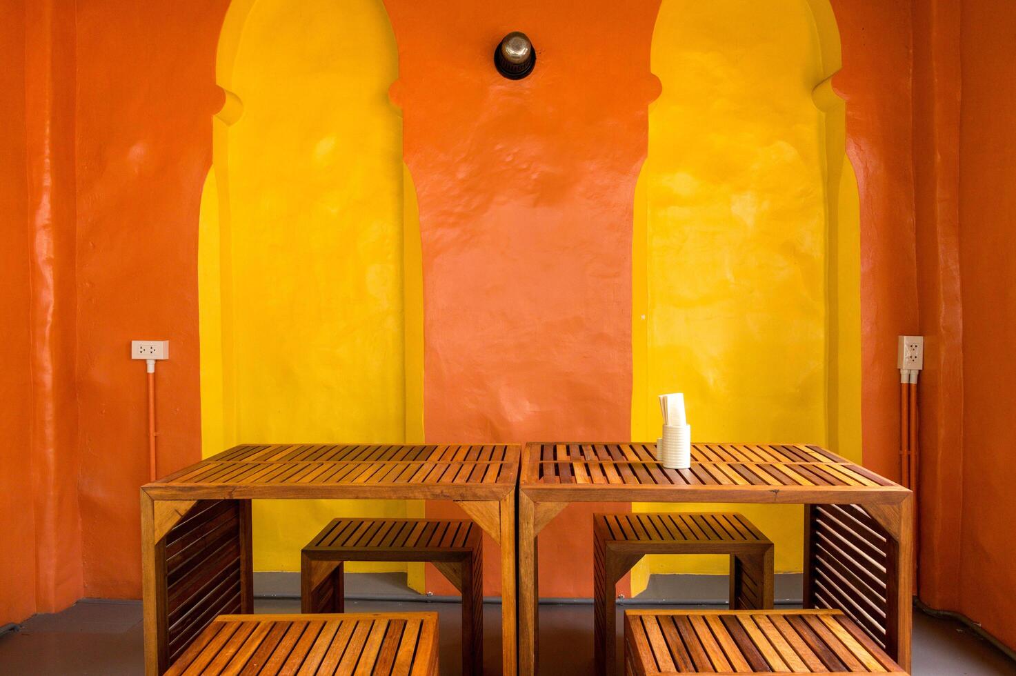 Bright room interior with yellow and orange walls featuring wooden tables and art, creating warm and inviting atmosphere with simple modern furniture and soft lighting photo