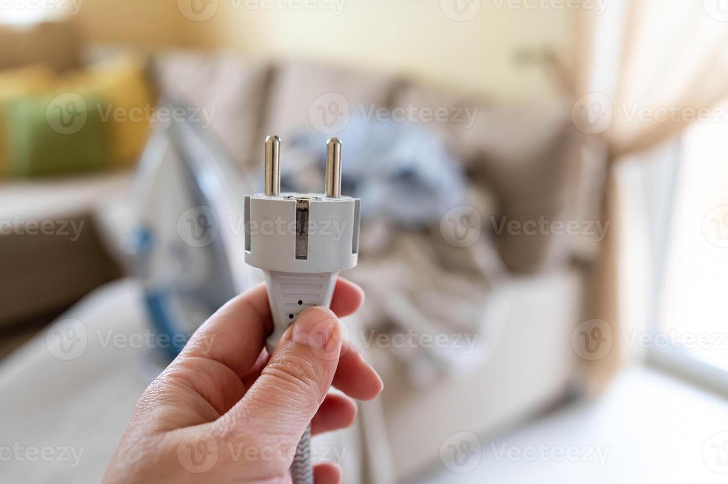 A person holding an electric plug in front of a couch photo