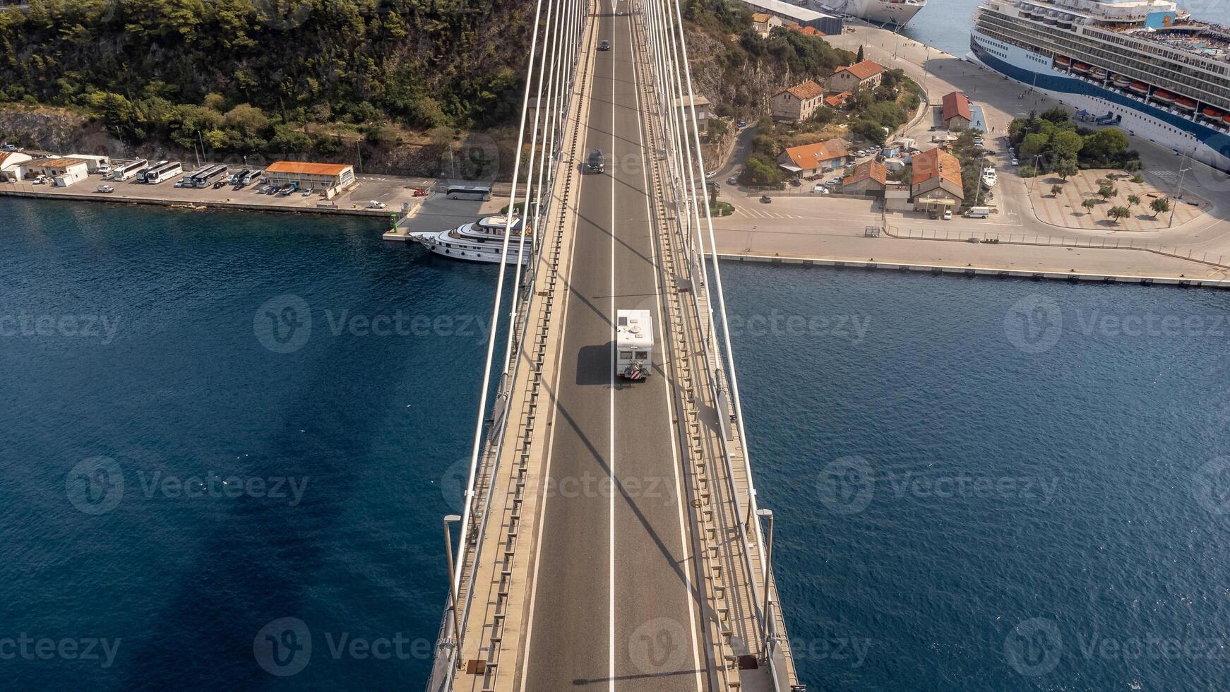 Top view of a suspension bridge over the Adriatic Sea with a traveling vehicle driving along the road photo