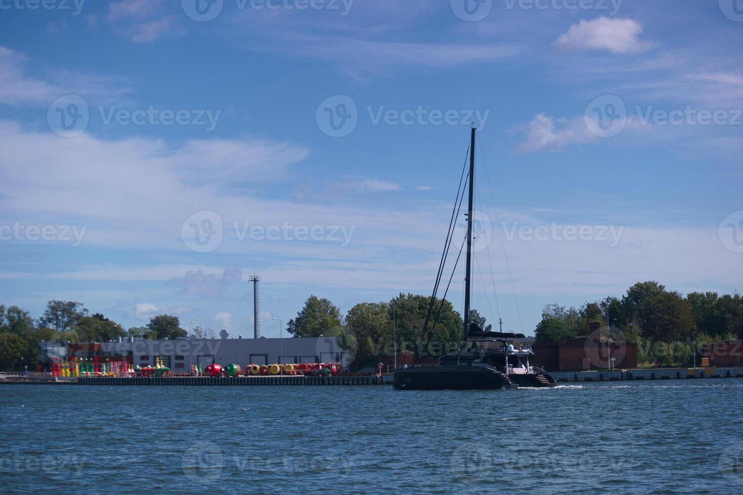 Sailing vessel glides through calm waters near colorful shoreline on a sunny afternoon photo