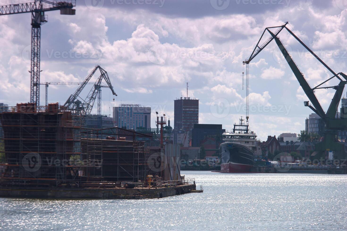 Construction and ship activity by the waterfront in a bustling city during the day with clouds in the sky photo