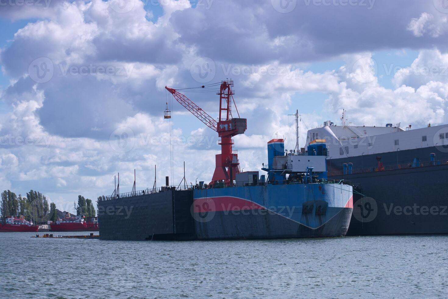 Cargo ship being loaded at a busy dock in the port with cranes and clouds in the backdrop photo
