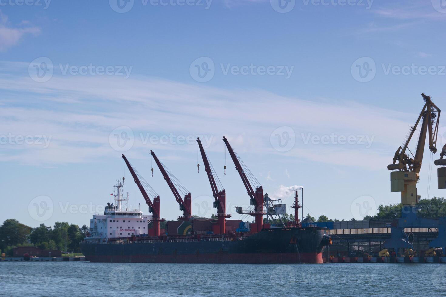 Cargo ship docks at busy port with large cranes lifting containers on a clear sunny day photo