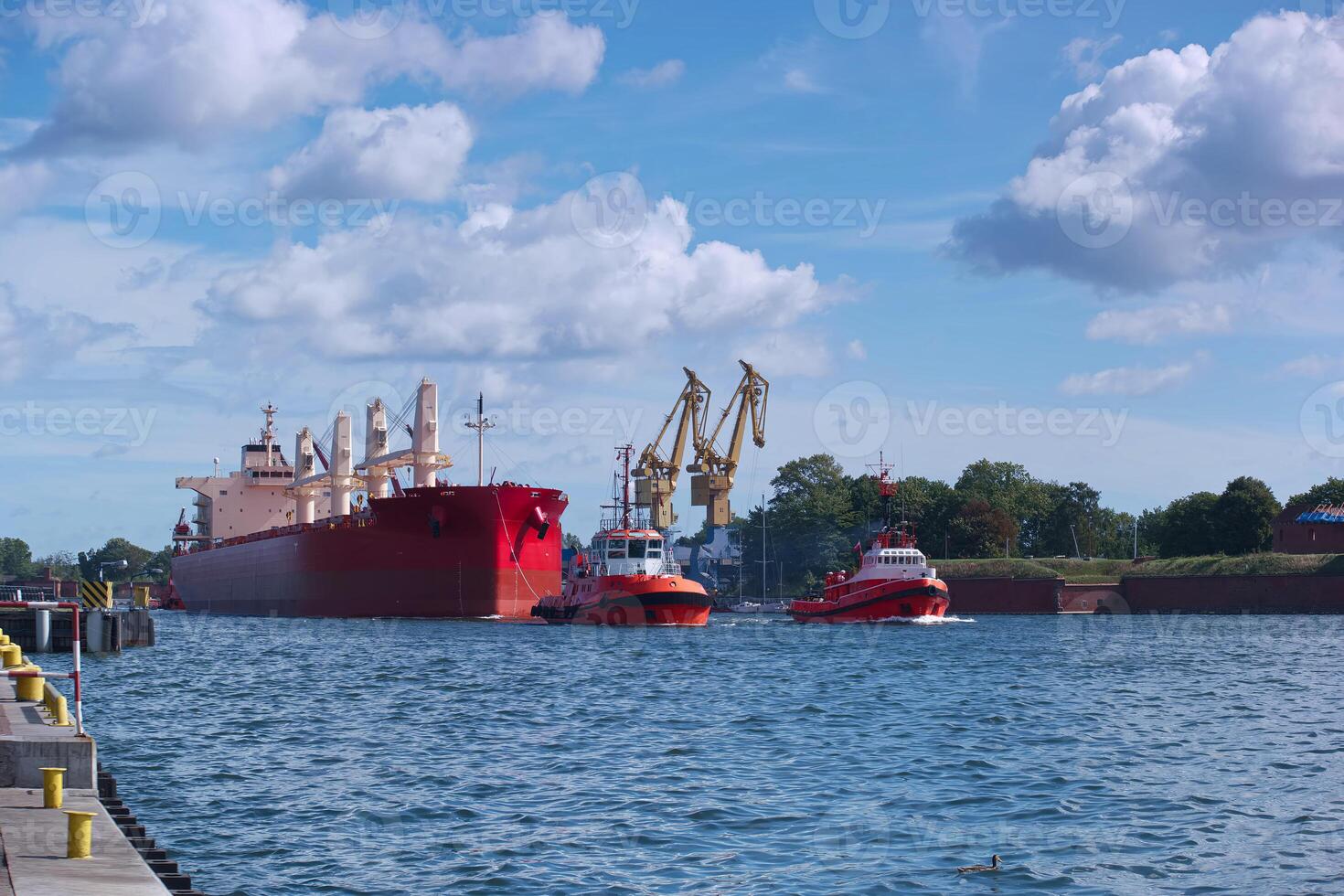 Cargo ships and tugboats maneuvering in a busy harbor under clear blue skies with a few clouds in the background photo