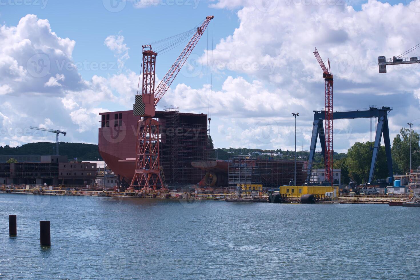Construction of a large ship at a shipyard in bright daylight with cranes and scaffolding present in the background photo
