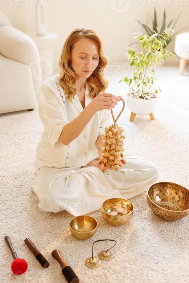 Calm woman practicing sound healing with seed rattle during spiritual meditation ritual at home. photo