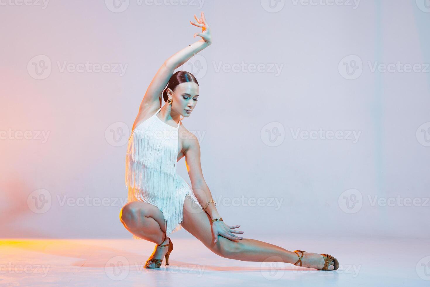 Female Latin dancer in dynamic pose wearing fringe dress under colorful studio lighting. photo