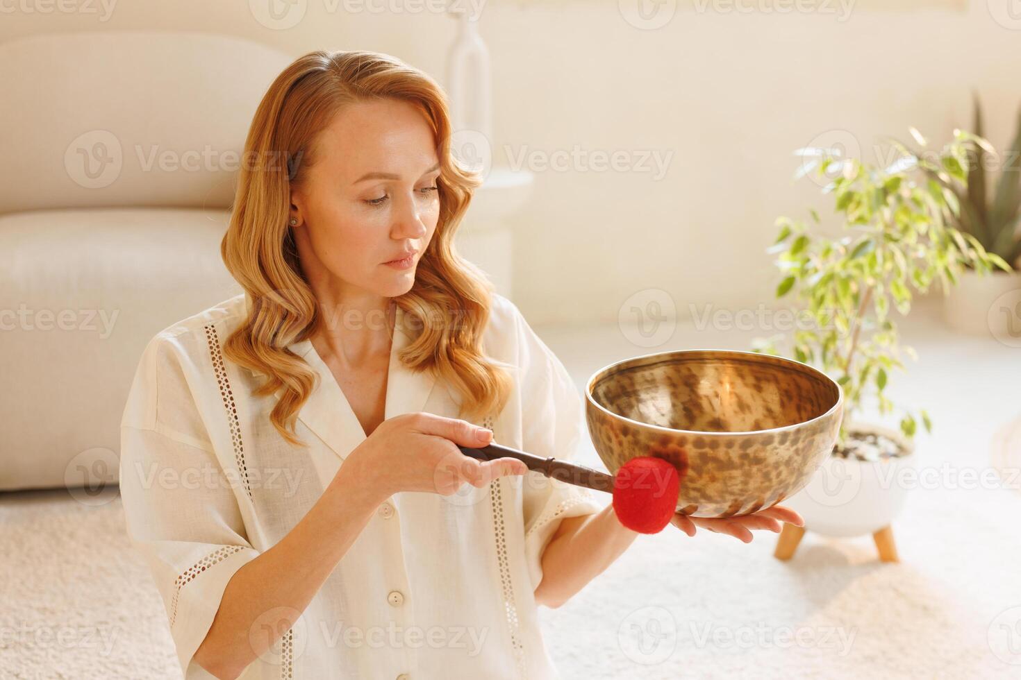 Woman practicing sound healing with Tibetan bowl in serene natural light at home. photo