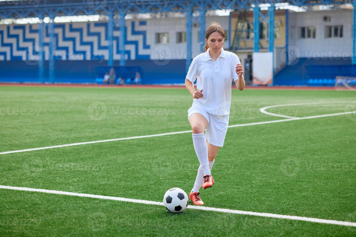 Young woman in white sportswear practices soccer ball control on green field. photo