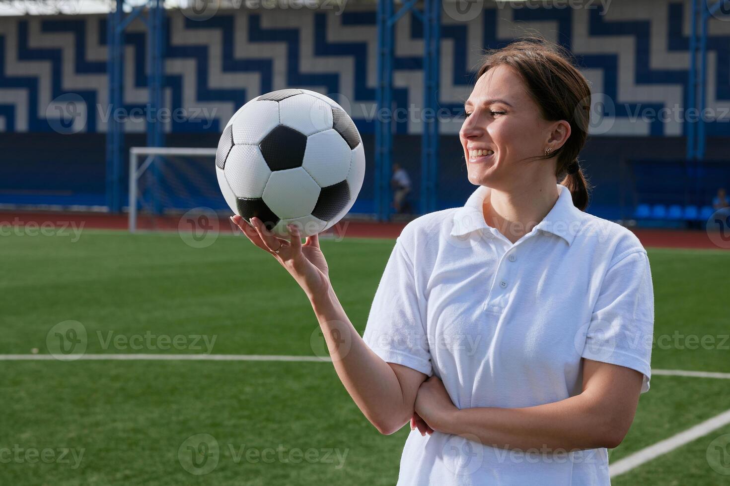 Young woman athlete balancing soccer ball on finger at stadium, smiling confidently. photo