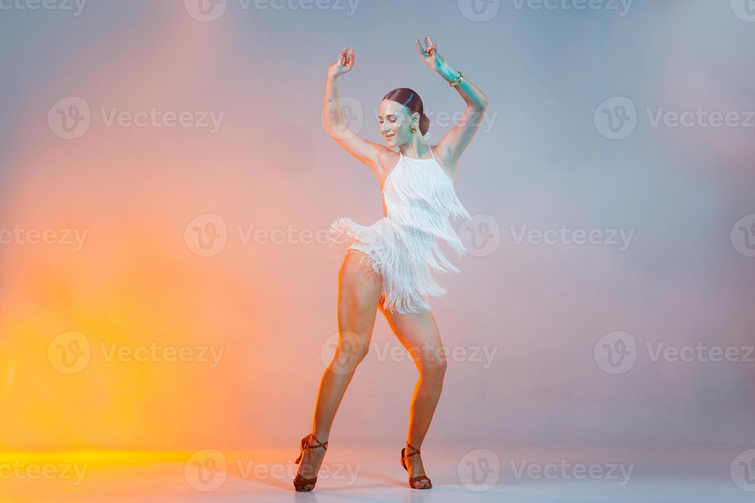 Smiling female dancer performing on stage in fringe dress with colorful studio lights and smoke. photo