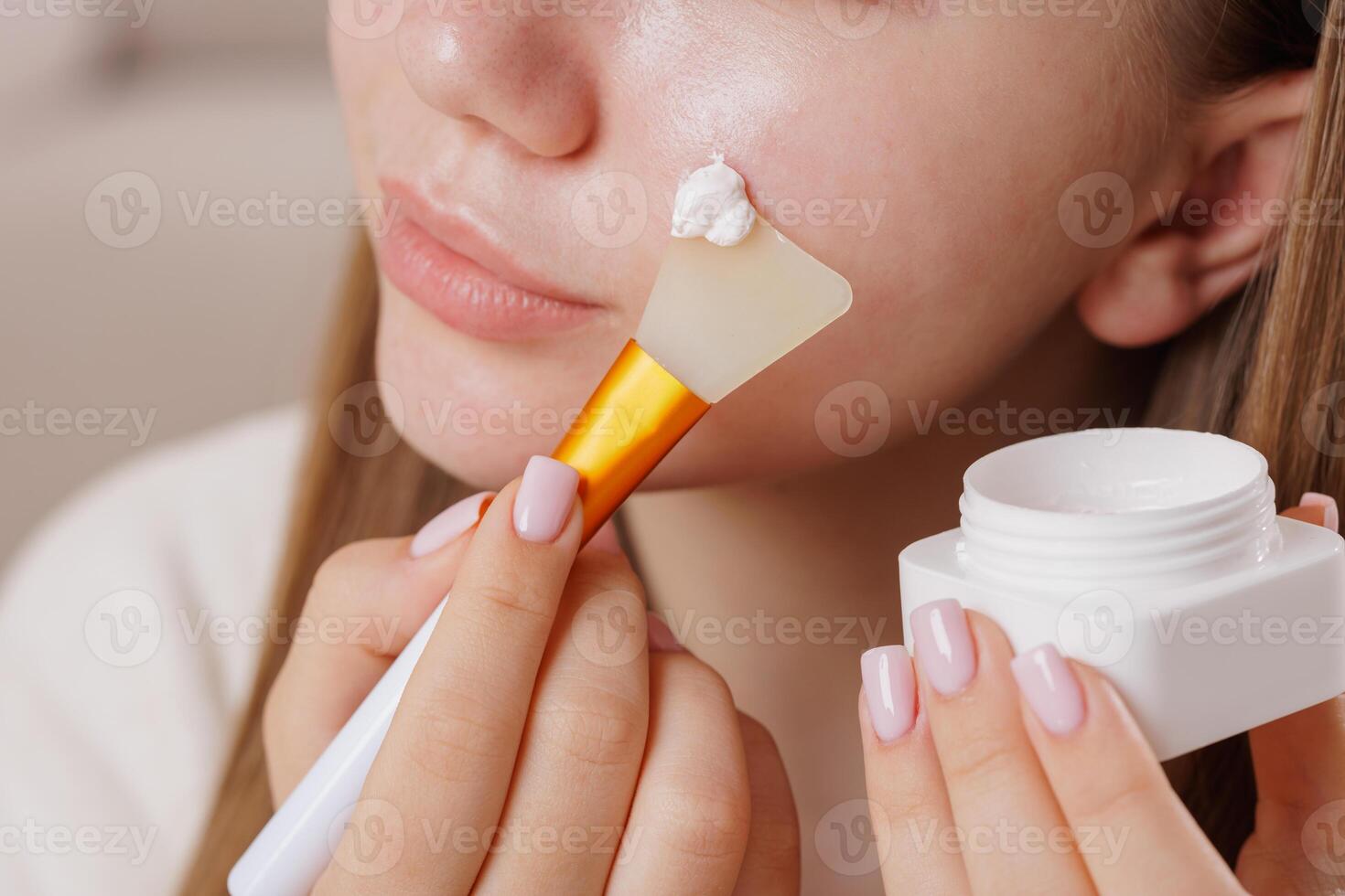 Girl using silicone brush to apply moisturizing cream to her cheek in beauty care process. photo