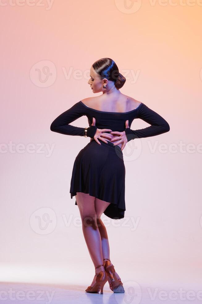 Back view of graceful dancer in black performing under pink-orange gradient studio lights. photo