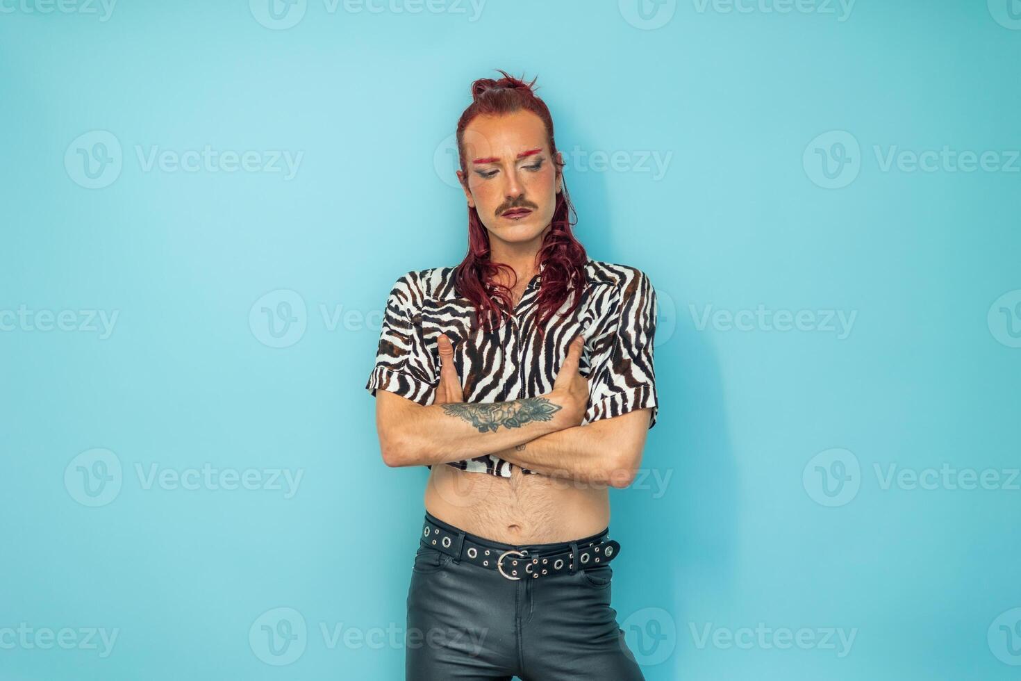 Non-binary person with arms crossed looking down on blue background photo