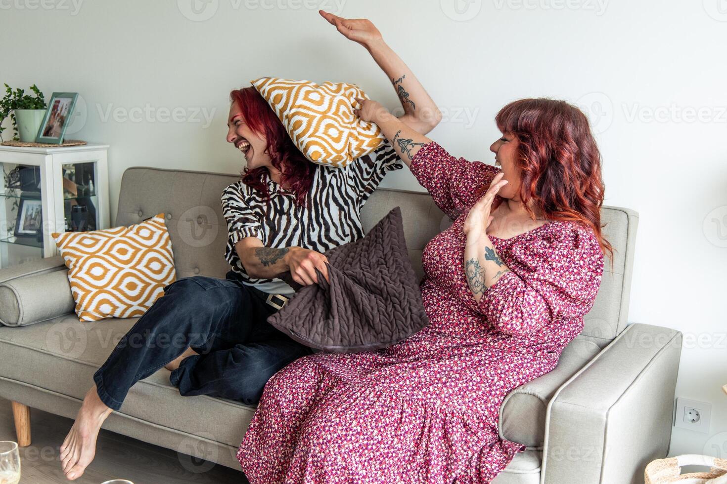 Two non-binary friends playing pillow fight on sofa at home photo