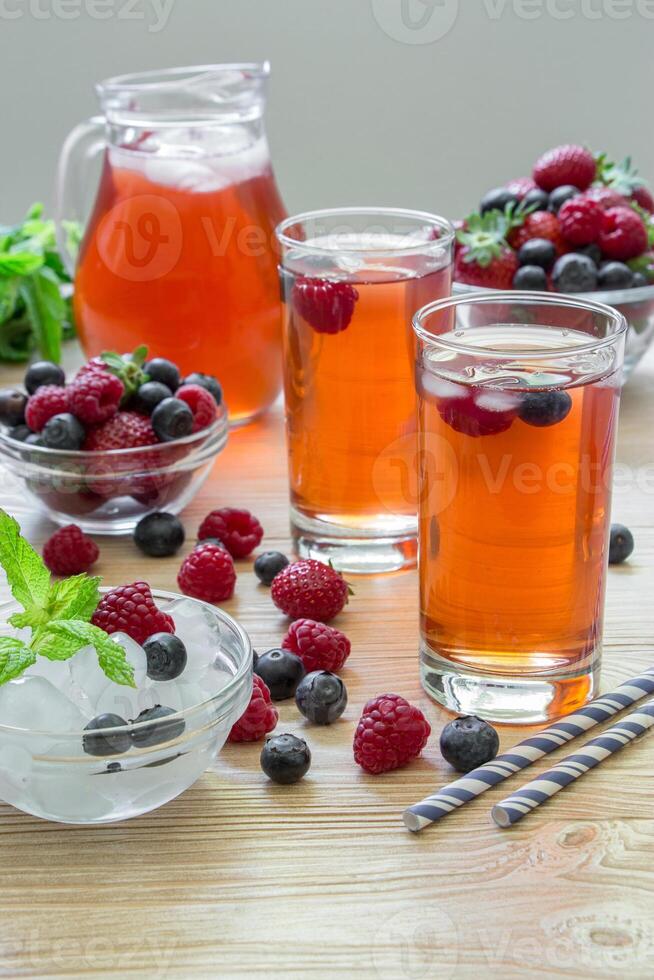 Colorful berry drinks filled with ice cubes and adorned with fresh berries create a vibrant display on a wooden surface, accompanied by mint leaves for added freshness. photo