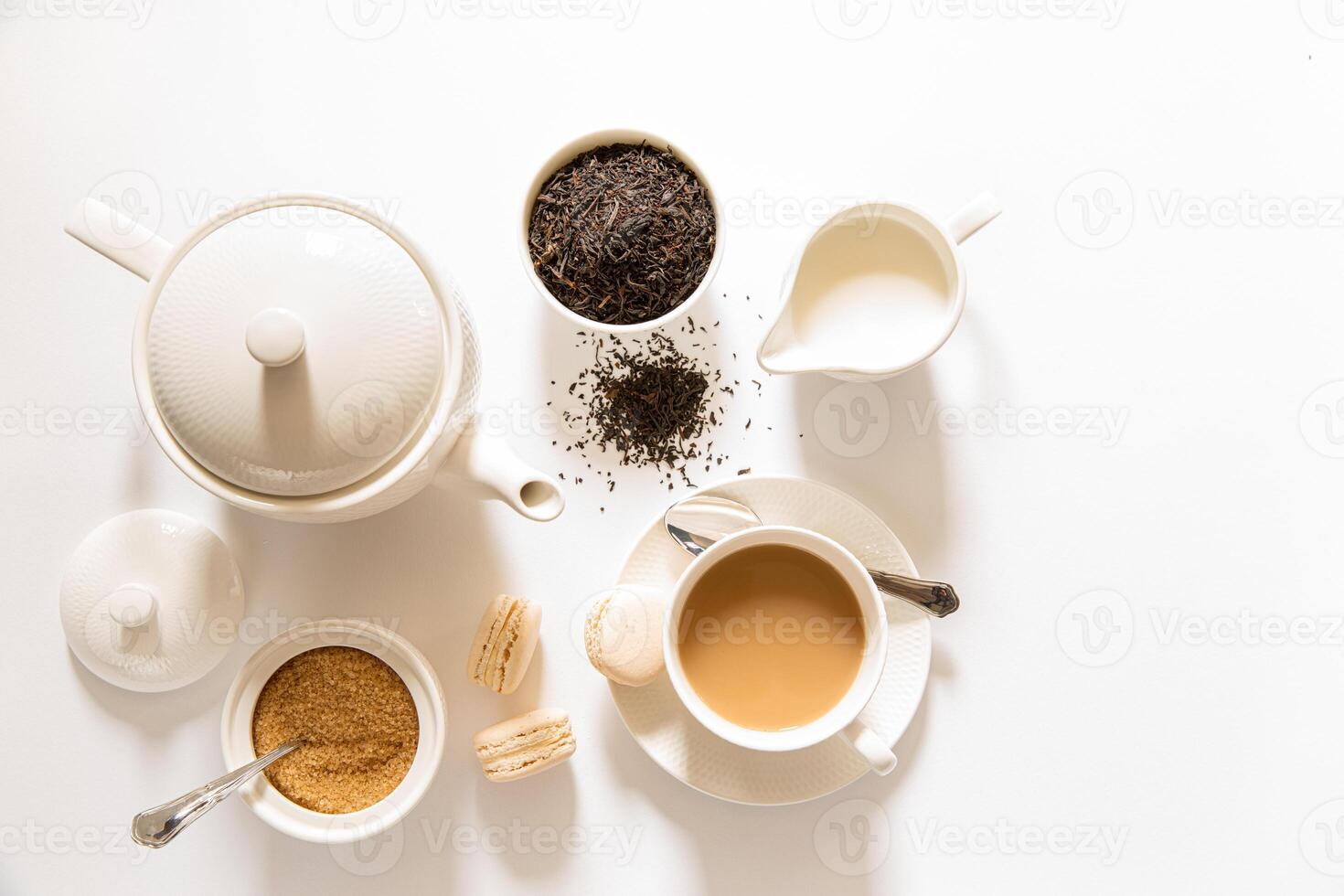 Inviting afternoon tea arrangement includes white tea pot, steaming cup of tea, bowl of sugar, and fresh macarons on minimalist table. Perfect for relaxation moment. photo