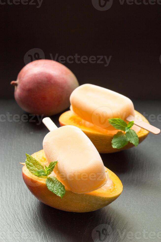 Enjoying creamy mango ice cream nestled in halved ripe mangoes, garnished with fresh mint leaves, ideal for a refreshing snack or dessert on a hot day photo
