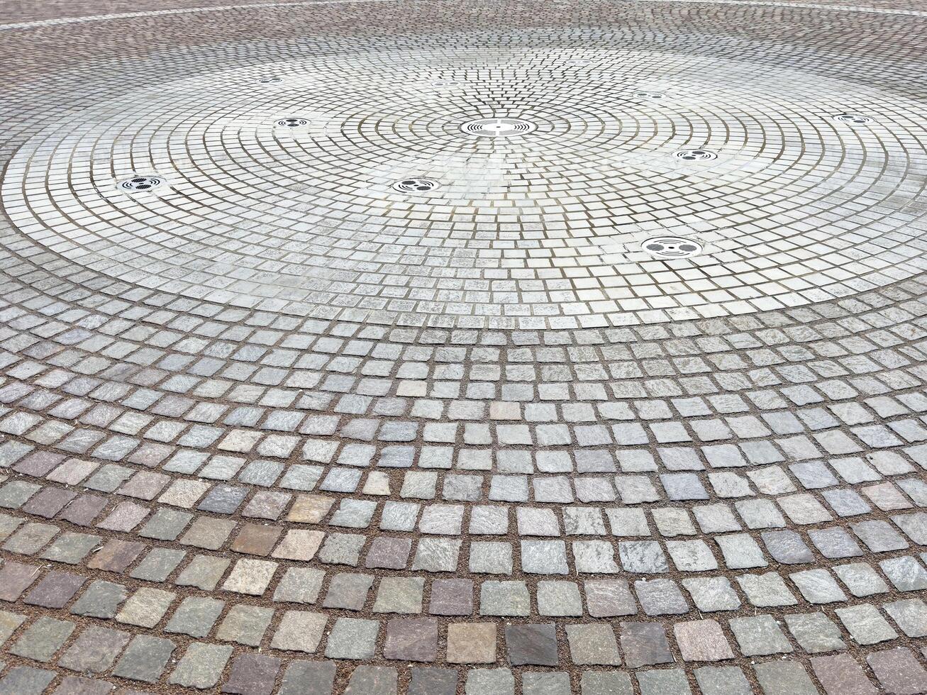 Circular stone pavement with intricate pattern and water fountains photo