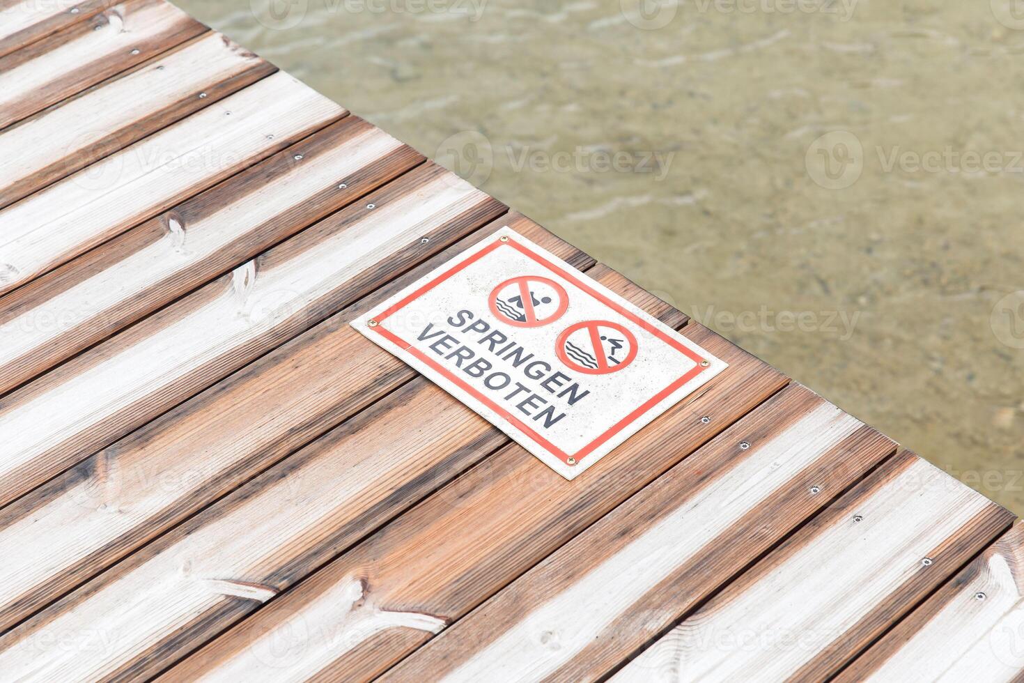 Dockside no jumping sign on wooden plank over clear water photo