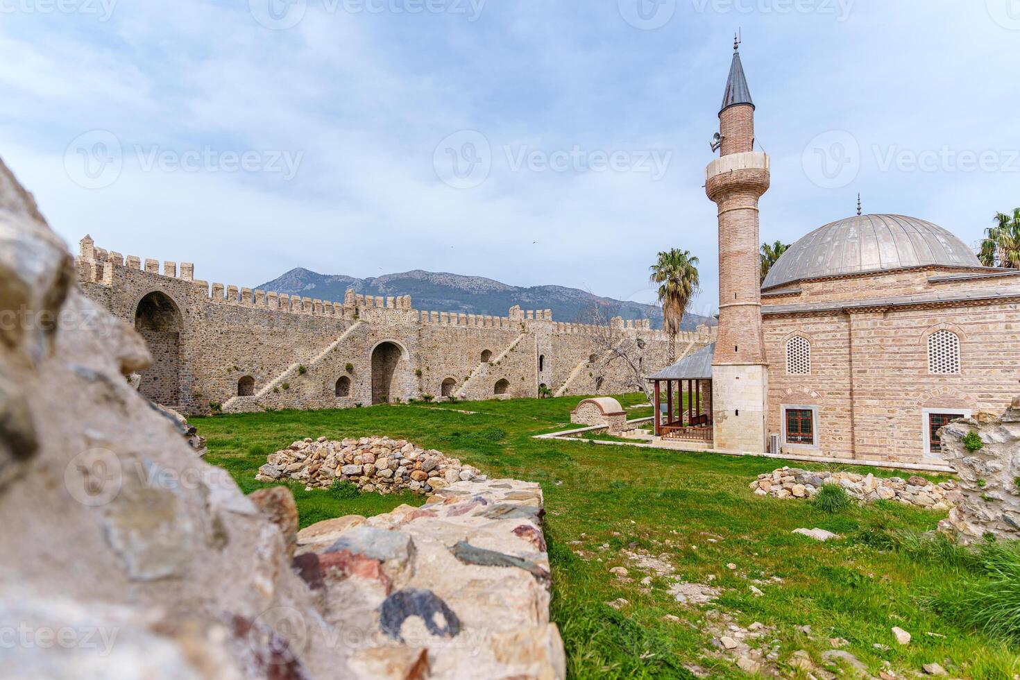 An ancient stone fortress and mosque stand gracefully amid a green field, epitomizing cultural history. photo