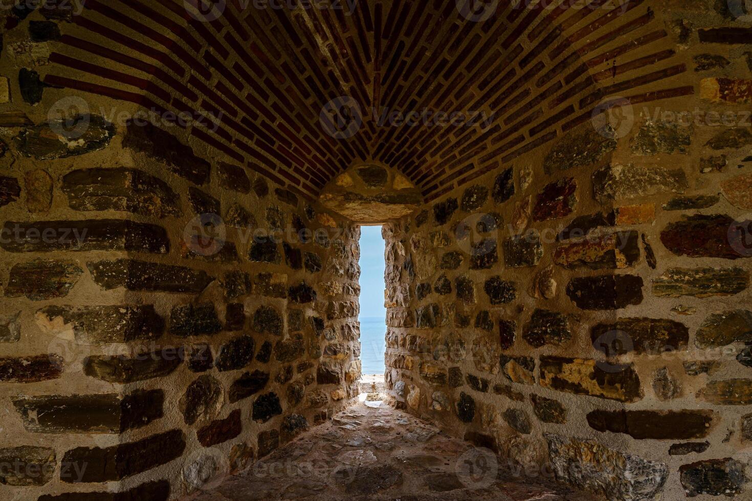 A well-worn stone wall with a narrow passage provides a picturesque view of a distant sea horizon photo