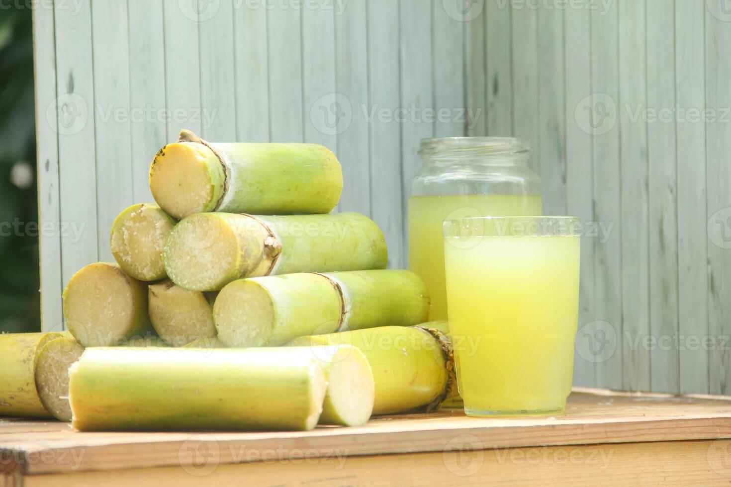A stack of green sugarcane with a glass of juice photo