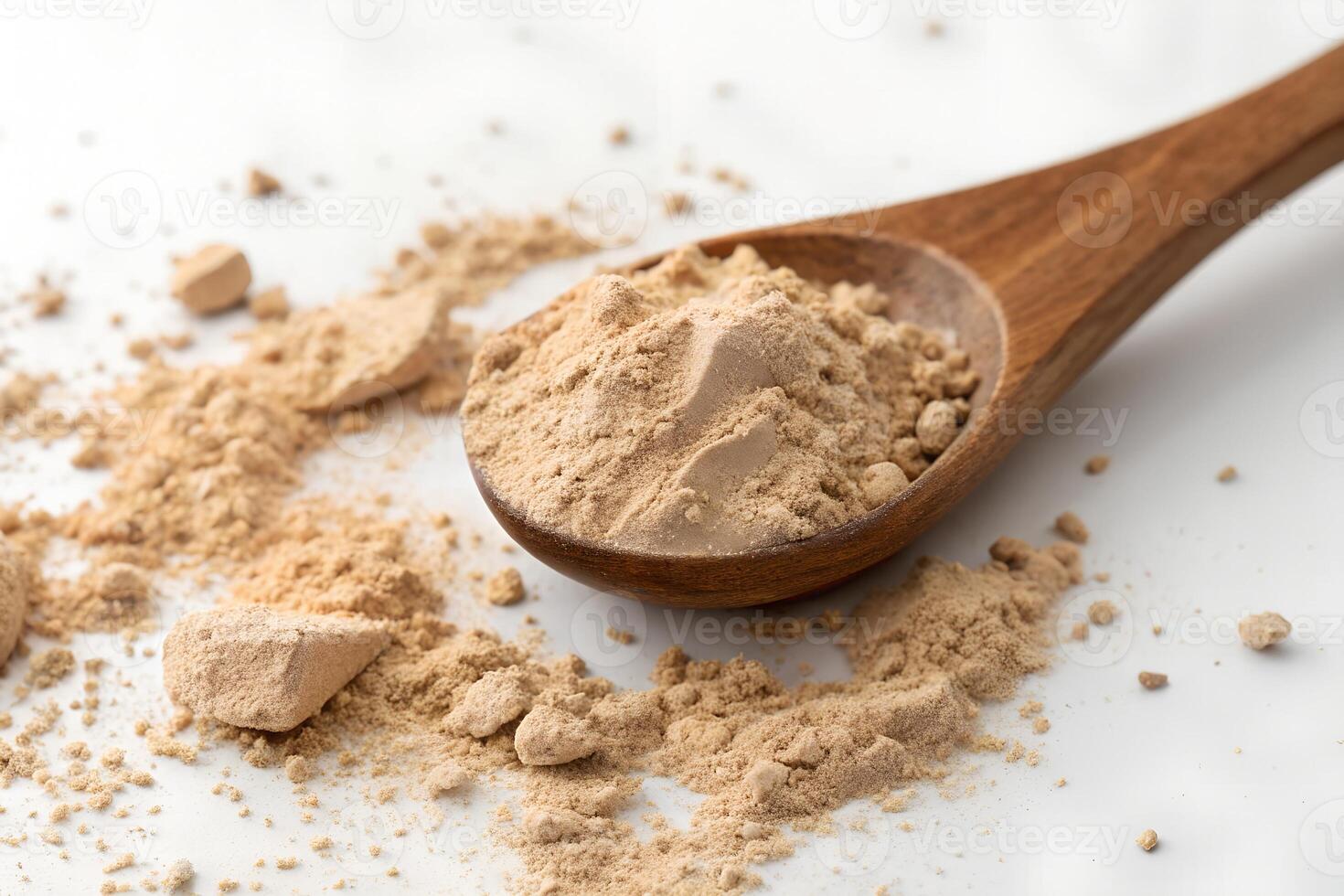 Golden powder fills a wooden spoon, with scattered granules on white surface photo