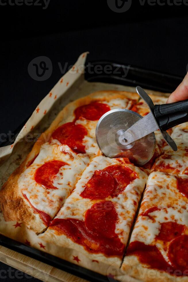 a person cutting a pizza with a pizza cutter photo