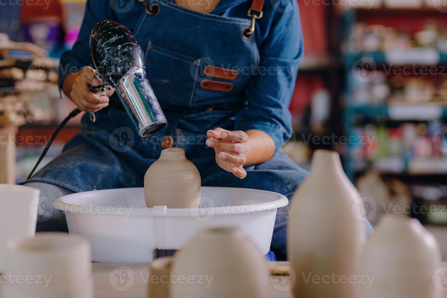 A woman is using a blow dryer to make some vases photo