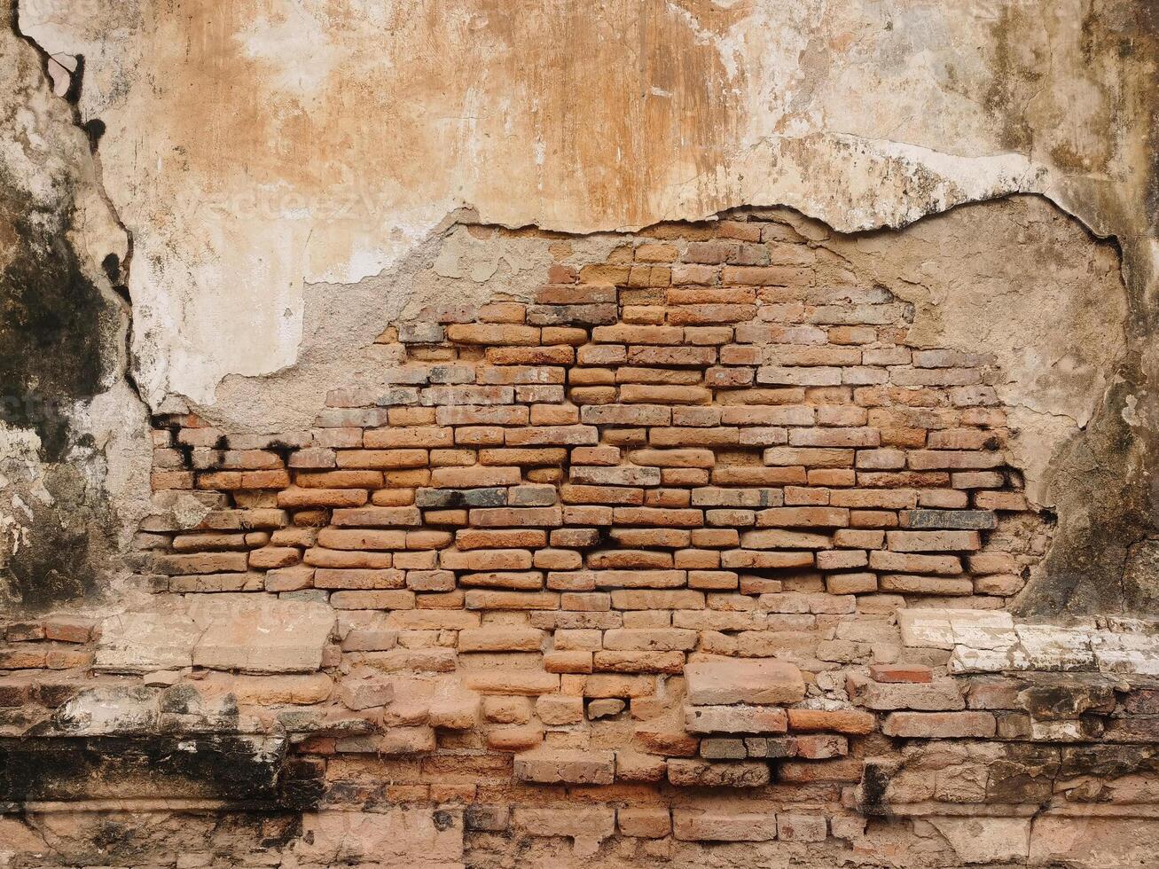 Picture of an old cement wall that has been cracked to reveal red bricks. photo