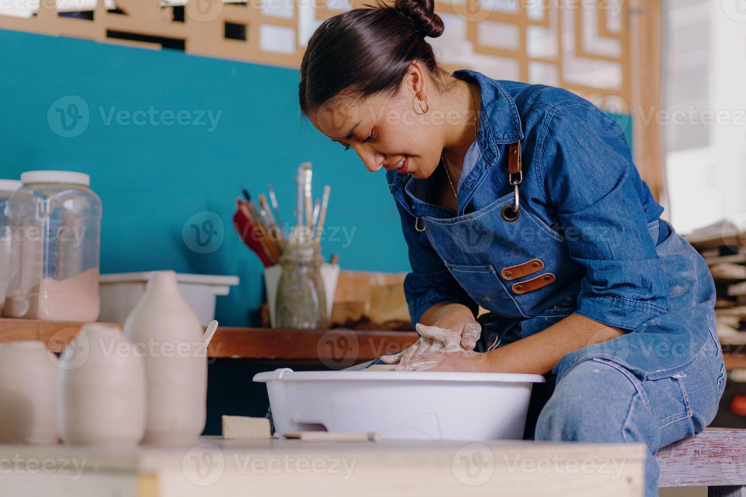 a woman in overalls is working on a pottery photo